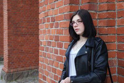 Young beautiful brunette girl in black jacket and  stands near wall of gothic church on summer