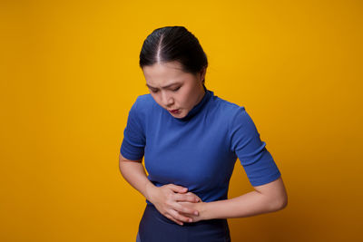 Young woman standing against yellow background