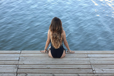 Rear view of woman wearing swimwear sitting on plank by river