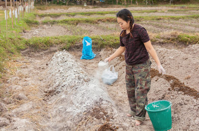 Woman putting fertilizer while standing on agricultural field