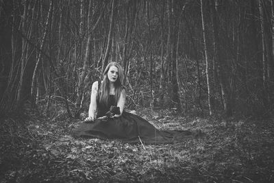 Young woman with flower while sitting on field against bare trees