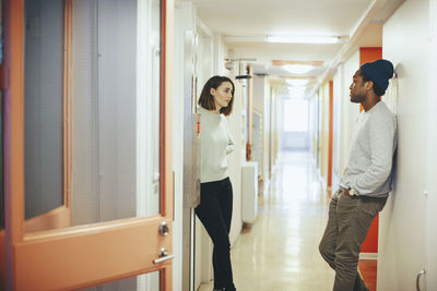 Young friends talking while standing in college dorm corridor