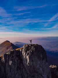 Man standing on rock by mountain against sky