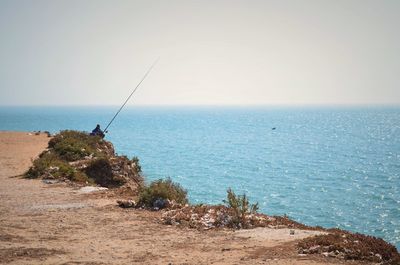 Man fishing by sea against clear sky