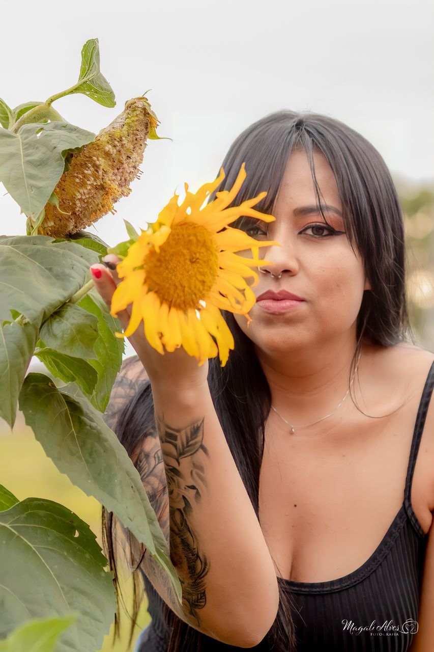 PORTRAIT OF YOUNG WOMAN WITH SUNFLOWER AGAINST YELLOW BACKGROUND