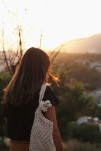 Rear view of woman standing against sky during sunset
