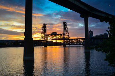 Silhouette bridge over river against sky during sunset