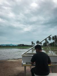 Rear view of man sitting on beach against sky