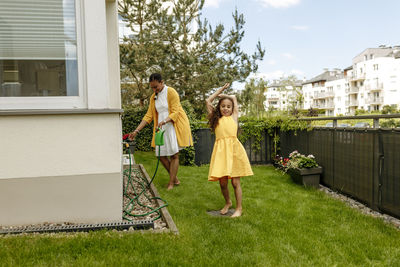 Happy girl with arms raised by mother holding watering can in garden