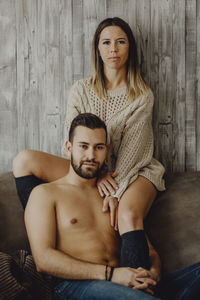 Portrait of young couple sitting against wall