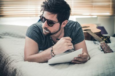 Young man writing on paper while lying on bed