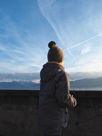 Rear view of person standing by retaining wall against sky