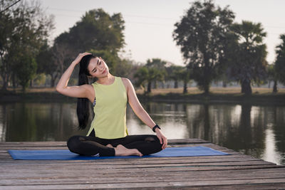 Full length of woman meditating by lake against trees