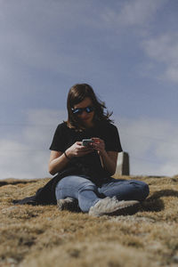 Woman using phone while sitting on land