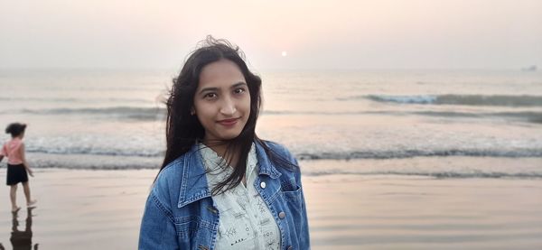 Portrait of beautiful woman standing on beach against sky during sunset