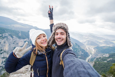 Portrait of cheerful couple standing on mountain during winter against cloudy sky