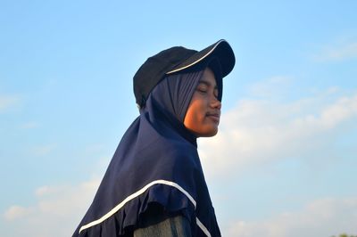 Low angle view of woman wearing cap standing against sky