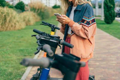 Young smiling woman rents city electric scooter using mobile app.