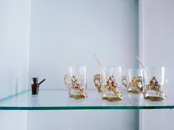 Drinking glasses on glass shelf against wall at home