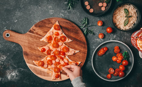 Children hand lay out sliced cherry tomatoes on a christmas tree cut from pizza dough 