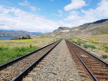 Railroad tracks leading towards mountain against sky