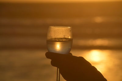 Close-up of hand holding drink against sky during sunset