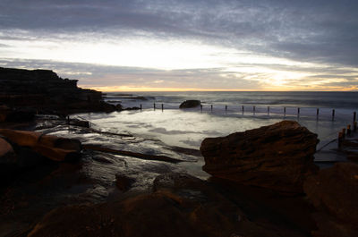 Rocks on beach against sky during sunset