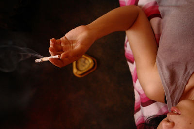 Midsection of woman holding cigarette while lying down