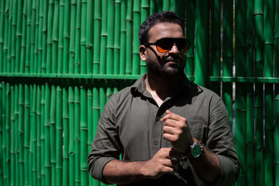 Man in sunglasses standing against wall during sunny day