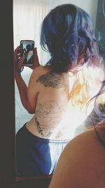 Rear view of woman photographing through smart phone at home