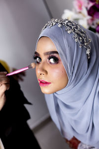 Cropped hand applying make-up on woman wearing hijab