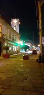 Illuminated street by buildings in city at night