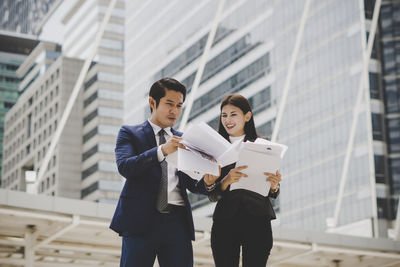 Low angle view of business people discussing documents while standing against building in city