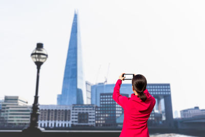 Rear view of woman standing by cityscape against clear sky