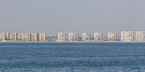 Sea by buildings against clear sky