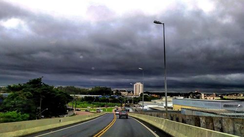 Vehicles on road against cloudy sky