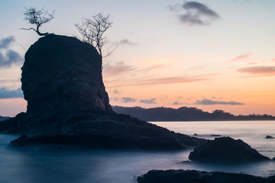 Rock formation in sea against sky during sunset