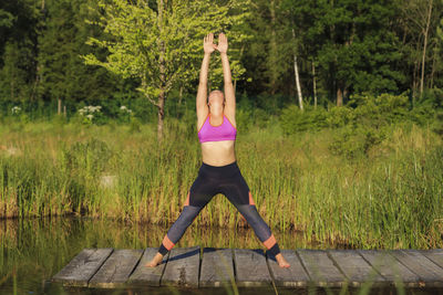 Full length of young woman with arms raised against trees