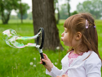Girl blowing bubble against trees