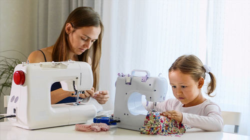 Cute girl using sewing machine with mother at home