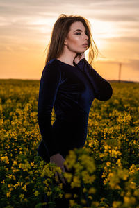 Beautiful young woman with yellow flowers on field during sunset