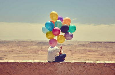 Rear view of woman with balloons sitting on sand