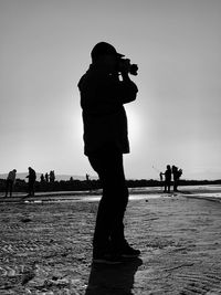 Silhouette man photographing on beach against sky
