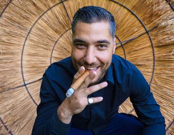 Portrait of smiling young man smoking cigar against thatched roof