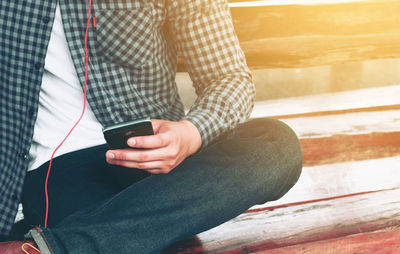 Midsection of man using phone while sitting on bench