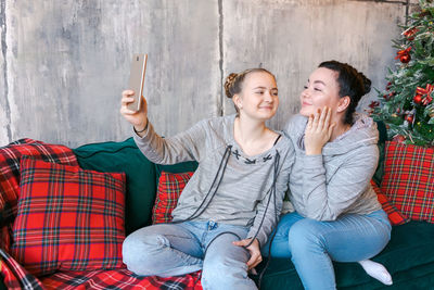 Two pretty young sisters in gray sweatshirts and blue jeans sit on couch near