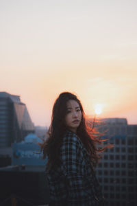 Beautiful young woman standing against sky during sunset