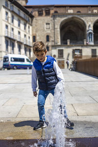 Full length of boy standing by fountain in city
