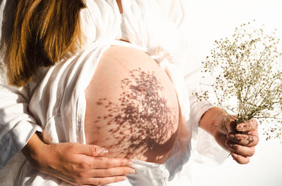  pregnant woman holding beautiful flowers having shadows on belly.pregnancy in spring,summer