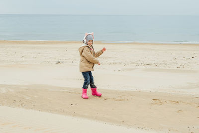 Little girl listens to music in children's pink headphones with cat ears and dances on the beach 